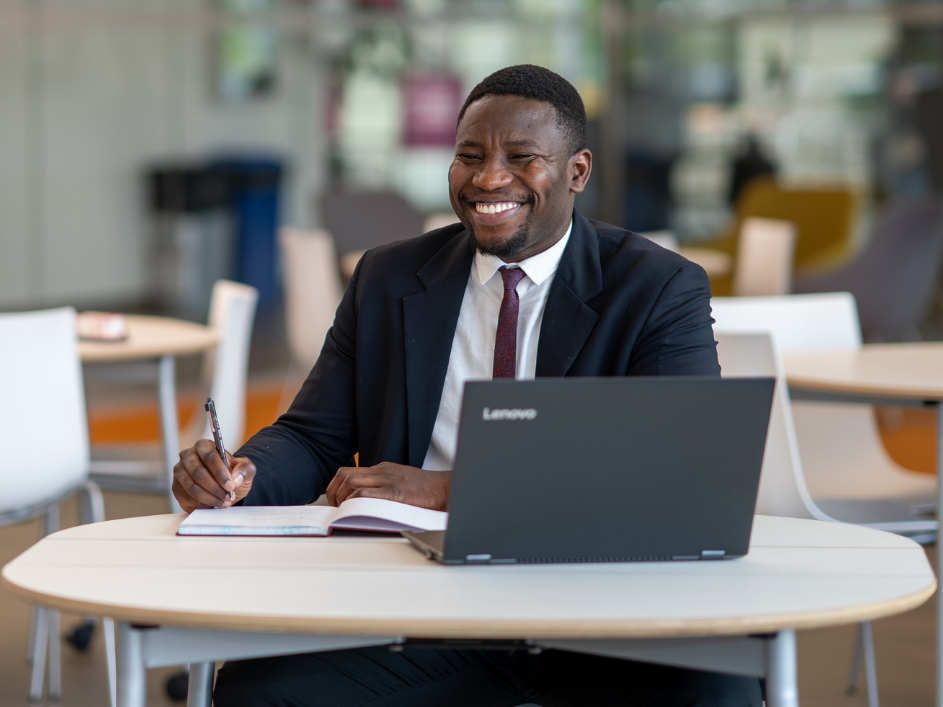 A smiling advisor sits at desk, writing notes.