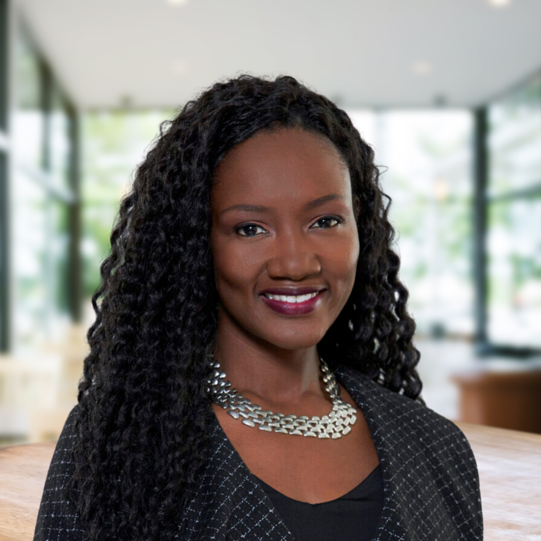 Headshot of Caroline Lule, a smiling woman with dark, curly hair, wearing a black striped blazer.